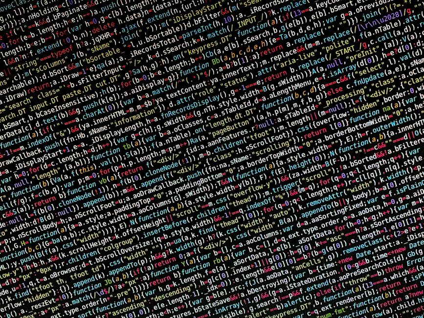 A close-up view of a person's hands typing on a MacBook laptop, displaying a dark-themed code editor with lines of colorful programming code. The laptop is placed on a dark surface, and the background